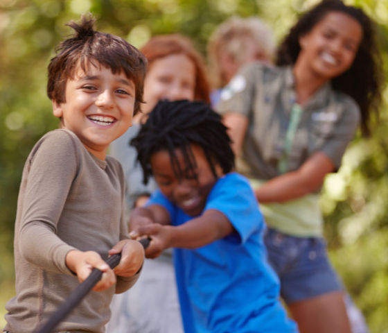 Kids smiling and playing tug-of-war outdoors at summer camp